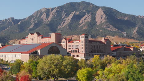 Aerial-up-close-view-of-CU-Boulder-campus-and-stadium-surrounded-by-green-and-yellow-fall-trees-with-the-rocky-flatiron-mountains-in-the-background-in-the-front-range-of-Colorado
