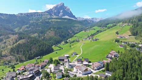 Nestled-within-the-expansive-green-meadows,-the-picturesque-village-of-Antermoia-offers-a-serene-retreat,-with-the-imposing-Peitlerkofel,-or-Sass-de-Putia,-majestically-standing-guard-in-the-backdrop