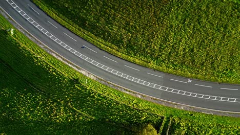 Drone-shot-of-cars-passing-on-rural-hill-corner