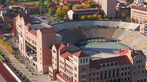 Aerial-up-close-view-of-CU-Boulder-campus-and-stadium-surrounded-by-green-and-yellow-fall-trees-with-the-rocky-flatiron-mountains-in-the-background-in-the-front-range-of-Colorado