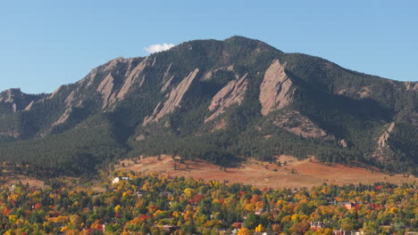 Aerial-up-close-view-of-Flatiron-mountains-in-Boulder-Colorado-surrounded-by-peak-fall-colors-of-green,-red,-and-yellow-trees