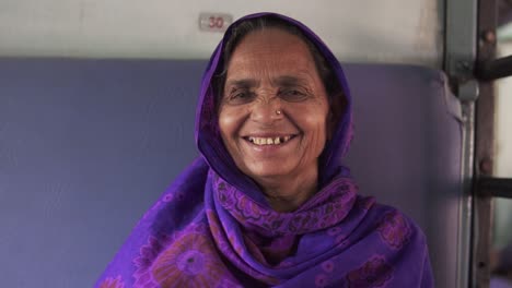 A-portrait-of-an-old-Indian-woman-traveling-on-a-train-in-India,-she-is-smiling-at-the-camera-and-is-happy-about-reaching-her-home-destination