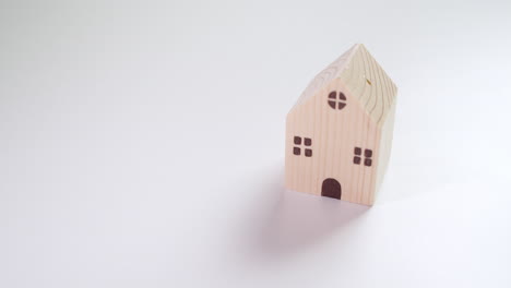 Wooden-toy-house-casting-shadow-on-the-table-and-then-the-lefthand-fingers-pushing-in-a-red-toy-sportscar-next-to-the-toy-house