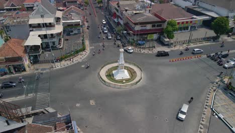 City-of-Yogyakarta-and-Tugu-monument-in-middle-of-roundabout-with-traffic,-aerial-view