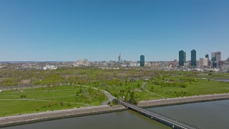 Aerial-flyover-Liberty-State-Park-with-high-rise-buildings-of-Jersey-City-in-background,-USA
