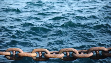 Strong-thick-rusty-metal-chains-and-blue-sea-background-in-two-time-slow-motion,-close-up-view