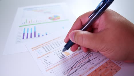Close-up-of-businessman's-hands-with-pen-working-at-office-desk-and-analyzing-dashboard-graphs-and-charts,-profit-report-checking