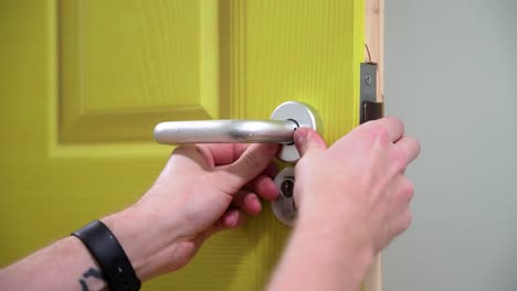 Tradesman-wearing-a-watch-fitting-and-installing-a-silver-door-handle-to-a-green-door-close-up