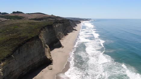 Aerial-video-of-Pescadero-Coast,-with-waves-at-the-beachside,-along-with-mountains-and-green-vegetation,-in-California,-USA