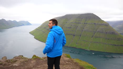 Man-enjoying-view-of-fjord-landscape-from-top-of-Klakkur-Mountain,-Faroe-Islands