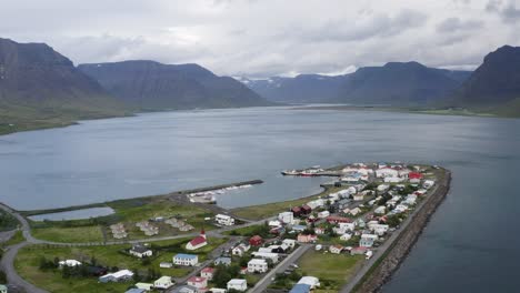 Aerial-backwards-shot-Flateyri-town-at-Westfjord-with-mountain-range-in-background,-Iceland