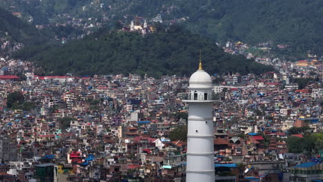 Kathmandu,-Nepal-Hat-Den-Weißen-Aussichtsturm-Dharrahara,-Die-Ganze-Hauptstadt-Ist-Zu-Sehen,-Mit-Grün,-Hügeln,-Landschaft,-Vergoldetem-Turm,-Urbanisierung,-Drohnenaufnahme,-Touristischer-Ort-4k