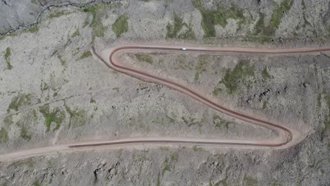 Aerial-top-down-shot-showing-car-on-curvy-road-in-mountains-of-Iceland,-Westfjords---Rocky-street-with-pattern