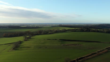 Drone-flying-cold-winter-green-fields-at-high-altitude-and-zoom-creating-parallax-movement-over-gentle-rolling-hills-in-north-yorkshire-countryside-in-England-and-blue-skies-with-some-cloud