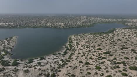 Vista-Aérea-De-Un-Hermoso-Paisaje-Y-Un-Lago-Rodeado-De-Desierto-De-Arena-Y-Matorrales-En-Sindh-Pakistán