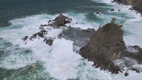 Aerial-view-of-tidal-waves-crashing-coral-island-with-huge-towering-rock