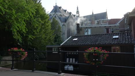Rauch-Kommt-Aus-Dem-Schornstein-Eines-Hauses-Mit-Der-Kirche-Sint-Janskerk-Im-Hintergrund-In-Gouda,-Niederlande