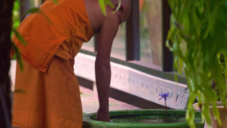 Buddhist-monk-in-orange-robe-smoking-cigarette,-cleaning-well-water