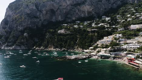 Wide-drone-shot-of-the-water-off-Capri,-Italy's-coast-with-buildings-lining-the-shore
