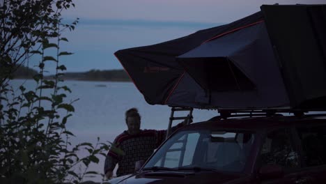 A-Man-Is-Going-Down-The-Car-Roof-Tent-Near-Lakeshore-A-Sunset