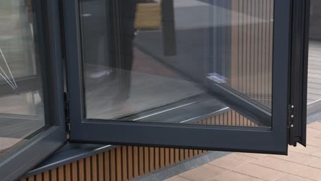 Close-up-shot-of-somebody-opening-sliding-bi-fold-patio-doors-in-slow-motion-on-luxury-wooden-garden-room-with-cladding-and-with-reflections-in-the-glass