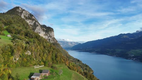 Aerial-backwards-flight-showing-greened-mountains-with-house-with-view-on-Walensee-Lake-in-Amden,-Switzerland-during-golden-hour