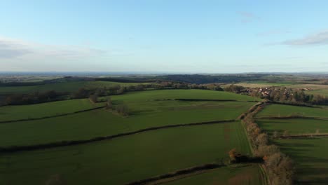 Drone-flying-over-cold-winter-green-fields-at-high-altitude-and-zoom-creating-parallax-movement-over-gentle-rolling-hills-in-north-yorkshire-countryside-in-England-and-blue-skies-with-some-cloud