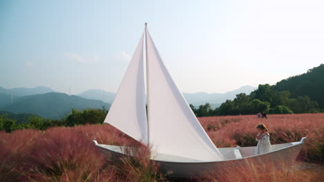 Little-Girl-Playing-Sailor-Inside-Wooden-Sail-Boat-at-Pink-Muhly-Grass-Field---Herb-Island-Farm-in-Pocheon