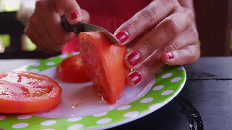 Female-hands-use-small-knife-to-cut-ripe-red-tomato-on-plate,-close-up