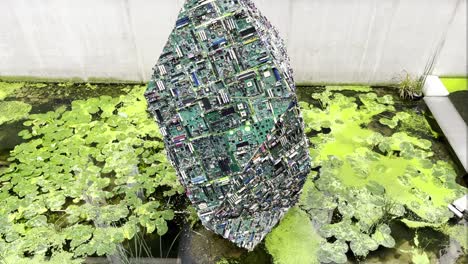 crystal-made-of-pc-motherboards-creating-shape-big-electric-stone-placed-in-small-lake-water-inside-leafs-and-greens-technology-and-nature-in-collaboration-together-cooperating-stone-wall-behind