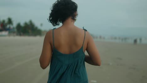 Medium-shot-of-a-young-indian-woman-dressed-in-a-green-dress-while-walking-on-the-beach-of-india-during-her-summer-vacation-in-the-evening