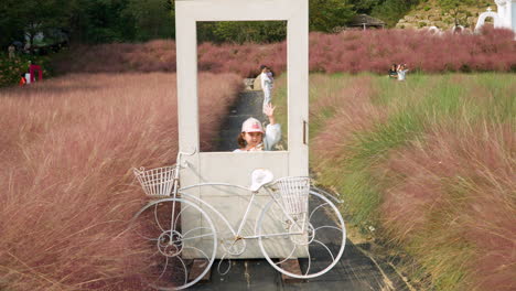 Child-Girl-Pose-at-Photo-Zone-with-Pink-Muhly-Grass-by-White-Door-and-Bicycle-in-Herb-Island-Pochen
