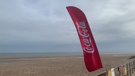 Eine-Coca-Cola-Flagge-Seufzt-Im-Wind-Am-Strand-An-Der-Strandpromenade