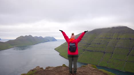 Eine-Glückliche-Frau-Hebt-Die-Hände,-Während-Sie-Vom-Klakkur-Berggipfel-Auf-Den-Färöer-Inseln-Auf-Das-Meer-Blickt