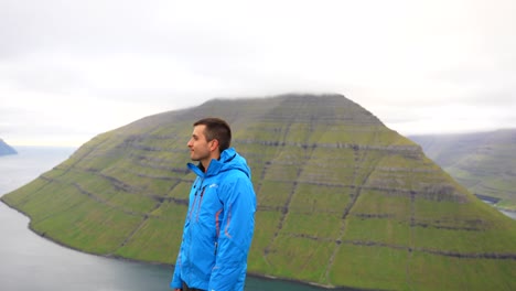 Un-Excursionista-Masculino-Sonríe-A-La-Cámara-Mientras-Disfruta-Del-Paisaje-En-La-Montaña-Klakkur,-Islas-Feroe.