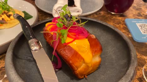Soft-brioche-bun-filled-with-delicious-meat,-pickled-red-onions,-yellow-sauce-and-microgreens,-delicious-food-on-a-plate,-fancy-restaurant,-4K-shot