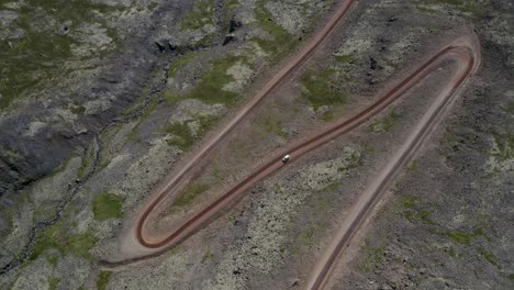 Aerial-top-down-shot-of-vehicle-driving-on-serpentine-road-on-rocky-Iceland-Island