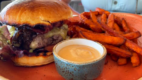 Yummy-cheeseburger-with-a-brioche-bun-and-sweet-potato-fries-with-spicy-mayonnaise-sauce,-fast-food-restaurant,-4K-shot