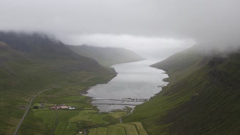 Aerial-approaching-shot-of-scenic-Sugandafjordur-Fjord-on-Iceland-between-green-hills-during-misty-day