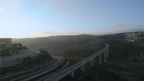 Huge-passenger-train-bridge-at-the-entrance-to-Jerusalem,-Israel-over-the-Kidron-Valley---the-modern-train-arrives-from-Tel-Aviv,-sunset-drone-shot
