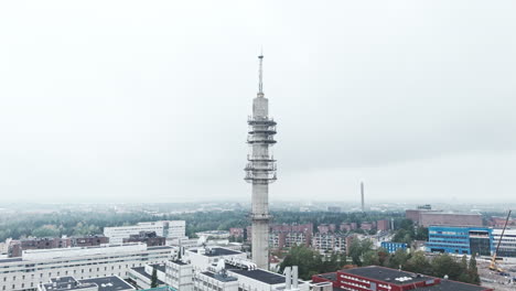 Aerial-wide-shot-of-a-bleak-industrial-concrete-television-and-radio-link-tower-in-Pasila,-Helsinki,-Finland-on-a-bright-and-foggy-day