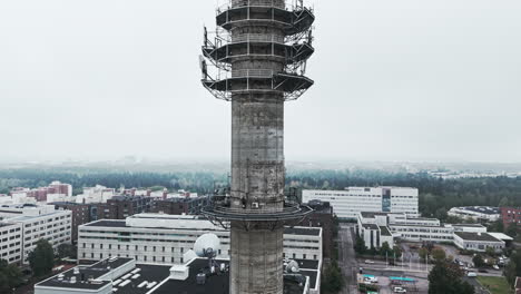 Aerial-medium-shot-of-a-bleak-industrial-concrete-television-and-radio-link-tower-in-Pasila,-Helsinki,-Finland-on-a-bright-and-foggy-day
