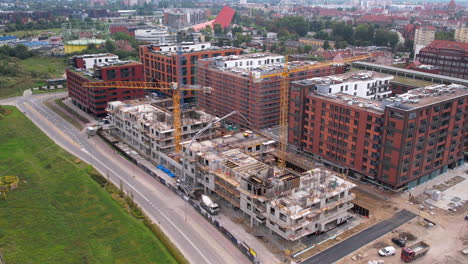 Aerial-view-of-a-bustling-construction-site-adjacent-to-modern-brick-apartment-buildings-in-Gdansk,-with-vehicles-navigating-the-city-road