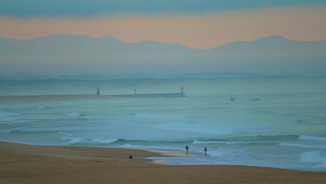 Cinematic-pan-follow-close-up-peir-toward-Biarritz-stunning-watching-early-morning-huge-waves-swell-surf-Hossegor-Seignosse-France-pink-purple-dusk-sunrise-on-beach-mountain-coast-landscape