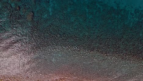 An-aerial-drone-shot-of-of-a-crystal-clear-ocean-shoreline-with-turquoise-water-and-small-pebbles