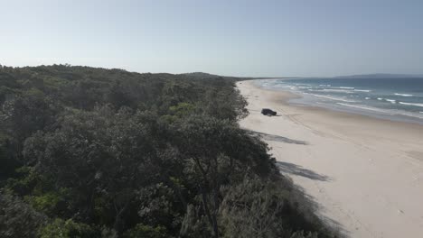 Low-jungle-flyover:-Truck-parked-on-endless-sand-beach,-QLD-Australia