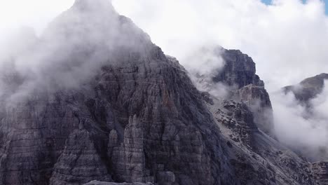 Aerial-of-steep-rocky-alpine-mountain-ranges,-foggy-clouds-around-peak,-epic-landscape-drone-scenery