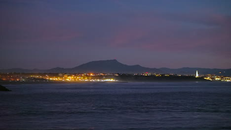 Cinematic-stunning-dramatic-evening-night-dusk-city-lights-lighthouse-shining-Biarritz-Hossegor-France-beach-mountain-coastal-landscape-Biarritz-Basque-Country-calm-water-bay-still-tripod