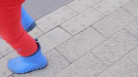 Little-child-walking-wearing-blue-shoes-in-city-landscape,-legs-shot