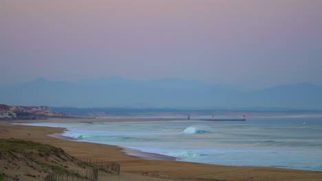 Cinematic-pan-close-up-toward-Biarritz-peir-stunning-watching-early-morning-huge-waves-swell-surf-Hossegor-Seignosse-France-pink-purple-dusk-sunrise-on-beach-mountain-coast-landscape